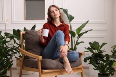 Evdeki koltukta bir fincan aromatik kahveli kadın.