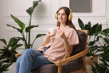 Elinde bir fincan aromatik kahve olan kadın evdeki koltukta müzik dinliyor. Metin için boşluk