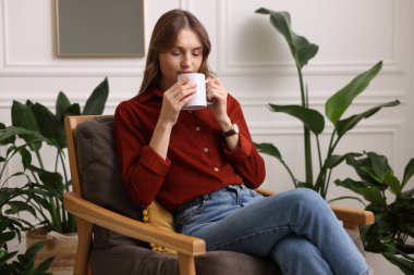 Evdeki koltukta bir fincan aromatik kahveli kadın.