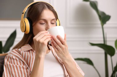 Elinde bir fincan aromatik kahve olan kadın evdeki koltukta müzik dinliyor. Metin için boşluk