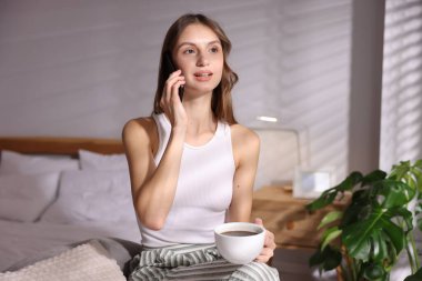 Evde kahve içen güzel bir kadın telefonda konuşuyor.