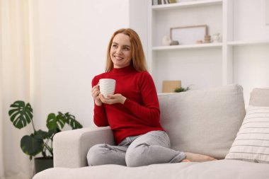 Evdeki kanepede bir fincan aromatik kahveyle güzel bir kadın.