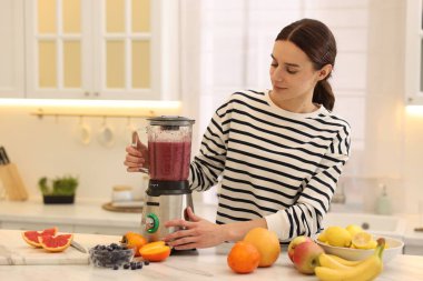 Mutfaktaki beyaz mermer masada blender ile nefis smoothie yapan bir kadın.