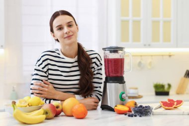 Beyaz mermer masada blender ve meyveli bir kadın var.