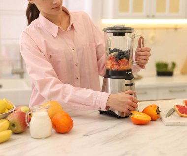 Mutfaktaki beyaz mermer masada blender ile nefis smoothie yapan kadın, yakın plan.