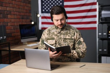 Askerlik. Ofisteki ahşap masada çalışan kulaklıklı asker.