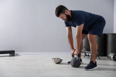 Güçlü adam spor salonunda kettlebell ile egzersiz yapıyor, mesaj için yer var.