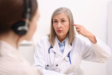 Duyma testi. Doktor içeride hastayla birlikte çalışıyor. Odaklanması gereken kulaklıklar takıyor.