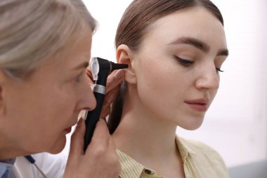 Duyma testi. Klinikte otoskopla hastanın kulağını muayene eden doktor, yakın plan.