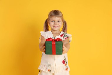 Sarı arka planda hediye kutusuyla gülümseyen küçük kız.