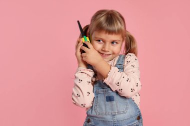 Pembe arka planda radyo kullanan tulumlu mutlu küçük kız. Metin için boşluk