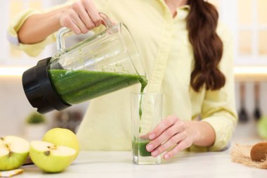 Kadın, beyaz mermer masada, blenderdan cama leziz bir smoothie dolduruyor.