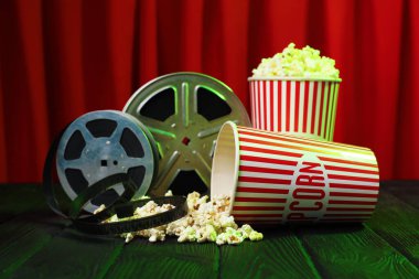 Kağıt bardaklarda patlamış mısır ve kırmızı perdelere karşı yeşil ahşap masada film makaraları.