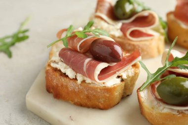 Krem peynirli lezzetli bruschettalar, prosciutto, zeytin ve roka gri masada, yakın plan.