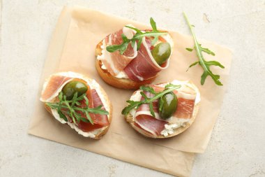 Krem peynirli nefis bruschettalar, prosciutto, yeşil zeytin ve roka, gri desenli masa, üst görünüm