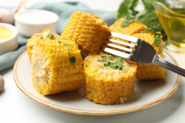 Beyaz masada servis edilen maydanozlu haşlanmış mısır koçanları.