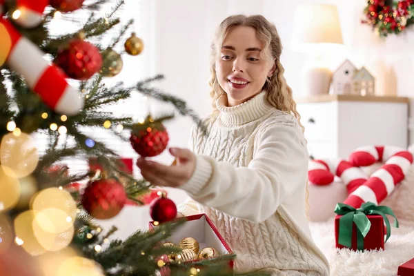 Evdeki Noel ağacına süveter giyen gülümseyen kadın güzel bir takı takıyor. Bokeh etkisi