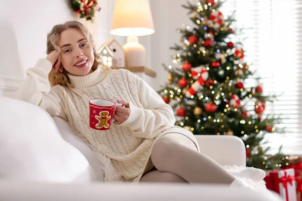 Süveter giymiş, elinde bir fincan sıcak içecekle gülümseyen kadın evdeki bulanık ışıklara karşı koltukta dinleniyor, mesaj için yer var. Mutlu Noeller ve mutlu yıllar.