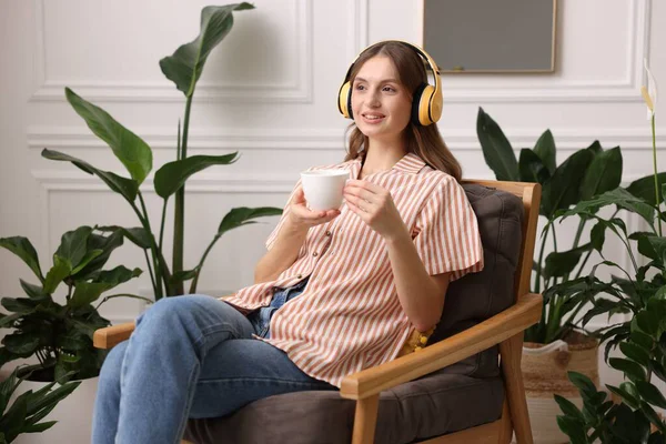 Elinde bir fincan aromatik kahve olan kadın evdeki koltukta müzik dinliyor. Metin için boşluk