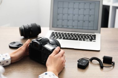 Ahşap masada dizüstü bilgisayarı, kamerası ve diğer ekipmanları olan profesyonel fotoğrafçı, yakın plan.