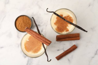 Lezzetli protein karışımı bardaklarda, tarçınlı ve vanilyalı kapsüller beyaz mermer masada, düz yerde.