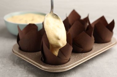 Kek yapıyorum. Gri masadaki kek tepsisine hamur koymak, yakın plan.