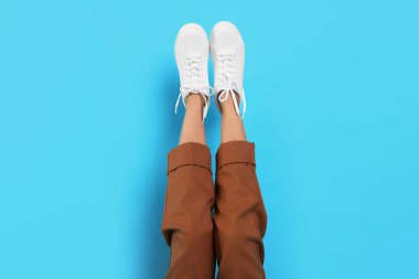 Açık mavi arka planda şık beyaz ayakkabılar giyen kadın, yakın plan.