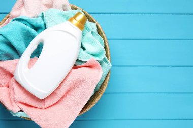 Açık mavi ahşap masa üzerinde havluyla çamaşır sepeti ve bir şişe deterjan, üst manzara. Metin için boşluk