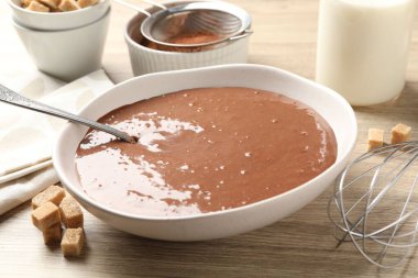 Kase içinde sıvı çikolata hamuru, süt, kakao tozu, esmer şeker ve çırpı, ahşap masada, yakın plan.