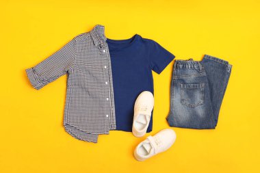 Düz kompozisyon, şık çocuk kıyafetleri ve sarı arka planda ayakkabılar.