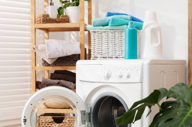 Çamaşır sepetinin içinde havlular ve çamaşır makinesinin üzerindeki deterjan şişeleri.