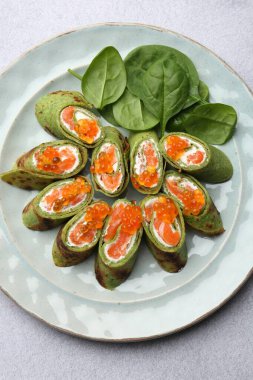 Somon, krem peynirli, kırmızı havyarlı ve açık gri masadaki yapraklı ıspanaklı krep.