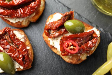 Krem peynirli lezzetli bruschettalar, güneşte kurutulmuş domatesler, biber biberi ve yeşil zeytinler masanın üstünde.