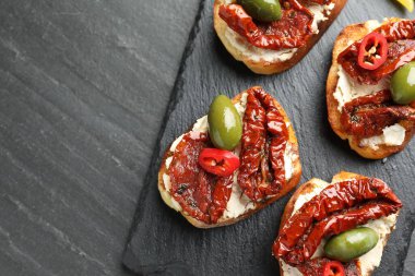 Krem peynirli nefis bruschettalar, güneşte kurutulmuş domatesler, acı biber ve gri dokuma masasında yeşil zeytinler, üst manzara. Metin için boşluk