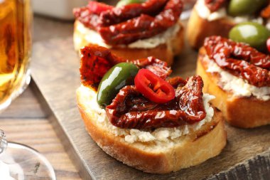 Krem peynirli lezzetli bruschettalar, güneşte kurutulmuş domatesler, kırmızı biber ve ahşap masada yeşil zeytinler, yakın plan.