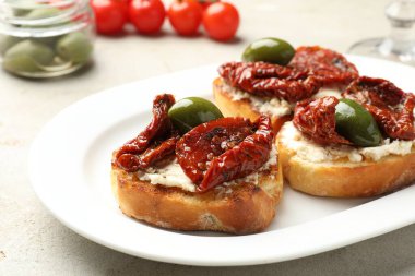 Krem peynirli lezzetli bruschettalar, güneşte kurutulmuş domatesler ve gri masada yeşil zeytinler, yakın plan.