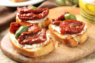 Krem peynirli lezzetli bruschettalar, güneşte kurutulmuş domatesler ve yeşil zeytinler masada, yakın plan.