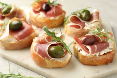 Delicious bruschettas with cream cheese, prosciutto, olives and arugula on table, closeup
