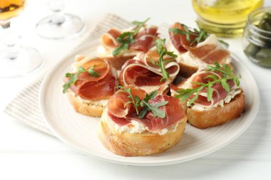 Krem peynirli nefis bruschettalar, prosciutto ve roka beyaz ahşap masada, yakın plan.