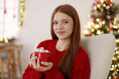 Evdeki bulanık ışıklara karşı elinde lokum dolu bir bardak sıcak içecek tutan güzel bir genç kız. Noel atmosferi