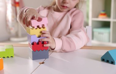 Oyun odasındaki beyaz masada oyuncaklarla oynayan mutlu küçük kız, yakın plan.