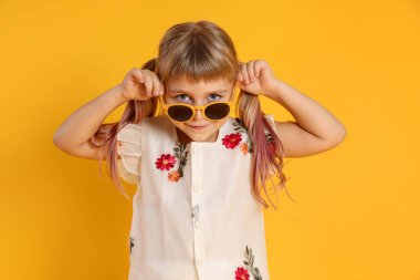 Sarı arka planda güneş gözlüğü takan sevimli küçük kız.