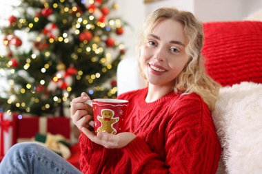 Evde bulanık ışıklara karşı elinde bir fincan sıcak içecekle gülümseyen kadın portresi. Mutlu Noeller ve mutlu yıllar.