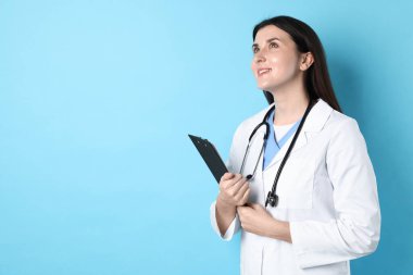 Açık mavi arka planda panosu ve steteskopu olan tıp üniformalı bir doktor.