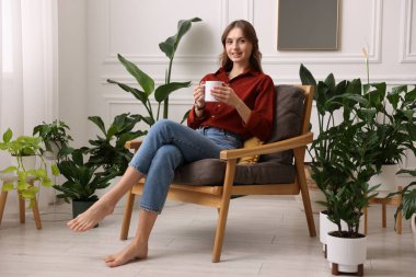 Evdeki koltukta bir fincan aromatik kahveli kadın.