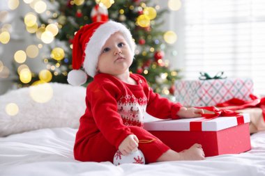 Noel Baba şapkalı şirin bir bebek, hediye kutusu ve evdeki yatakta takı. Noel sezonu