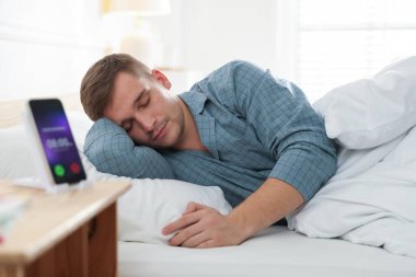 Adam yatakta esniyor ve akıllı telefon ve alarm saati uygulaması içeride.