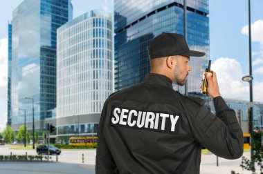 Üniformalı güvenlik görevlisi dışarıdaki binaları gözetliyor.