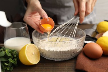 Kadın kaseye yumurta eklerken ahşap masada kek için hamur işi, yakın plan.