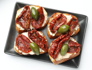 Krem peynirli lezzetli bruschettalar, güneşte kurutulmuş domatesler ve beyaza izole edilmiş yeşil zeytinler.